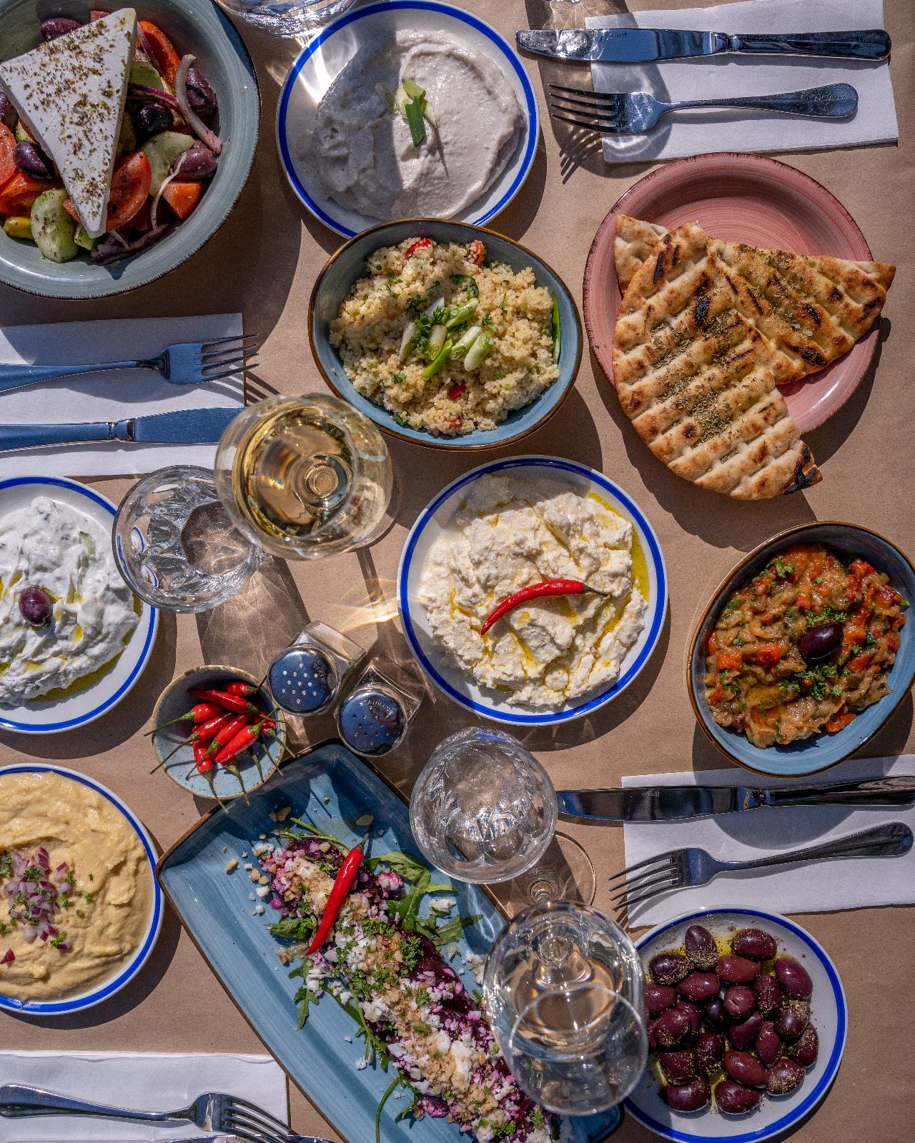 Griechische Meze mit Salat, Dips und Fladenbrot auf einem gedeckten Tisch